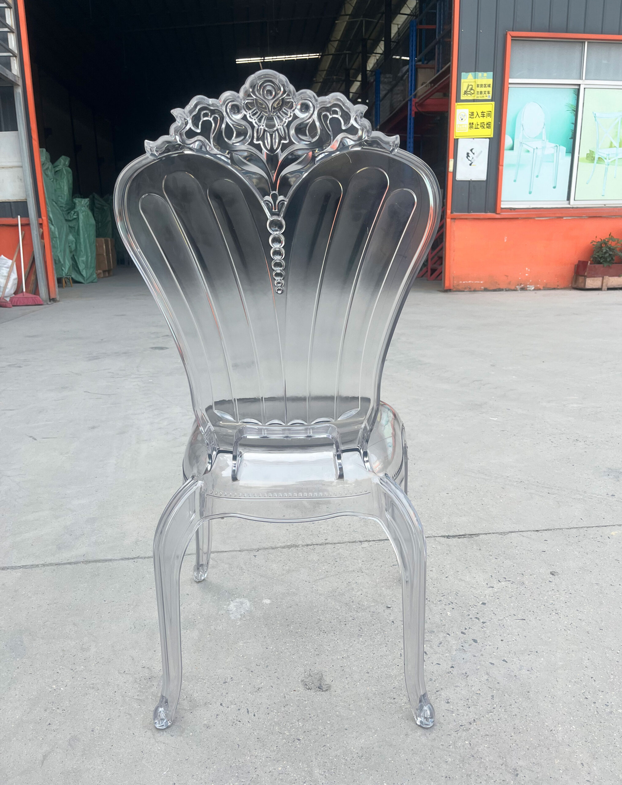 Angled side and back view of a transparent Baroque-style acrylic banquet chair with curved legs and floral backrest