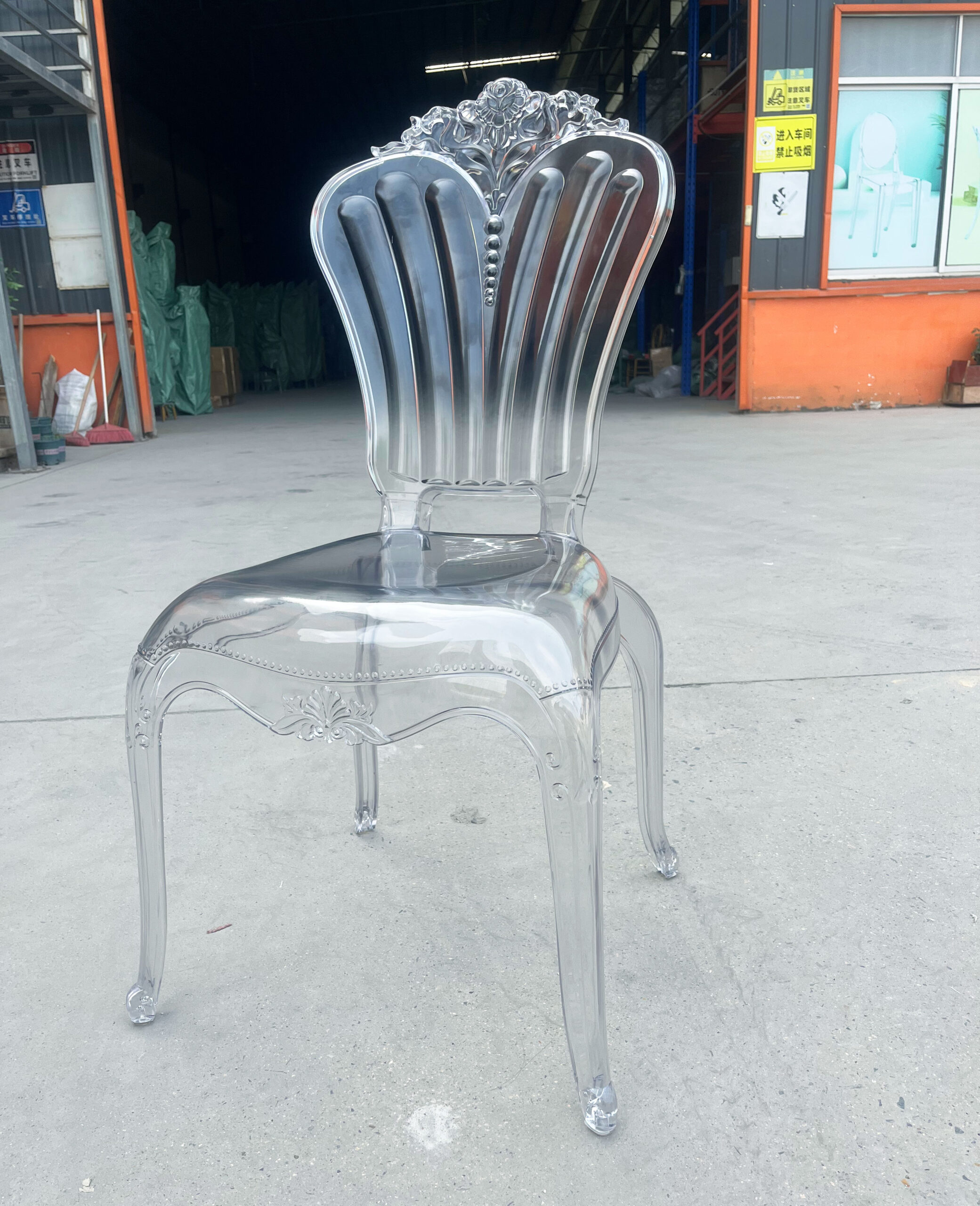 Front angle of a transparent acrylic banquet chair with Baroque-style floral backrest and elegant curved legs