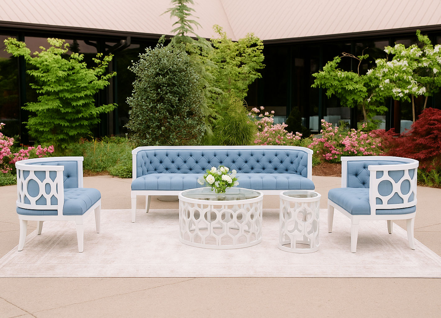 Outdoor wedding lounge setup featuring a white wood frame sofa and chairs with blue tufted upholstery, matching carved round coffee tables, and floral centerpiece.