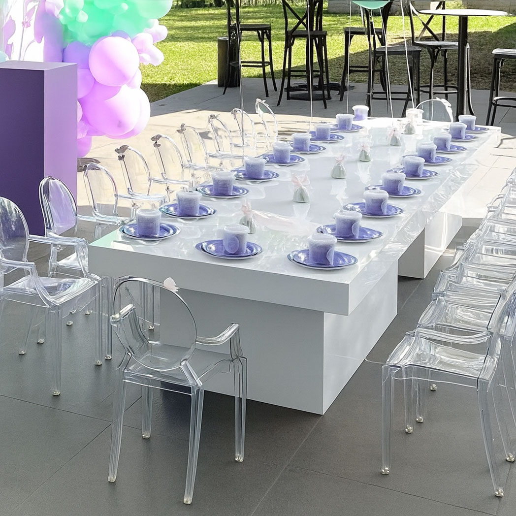 Modern white kids event long table with transparent chairs and lavender plates arranged outdoors for a children’s birthday or party setup