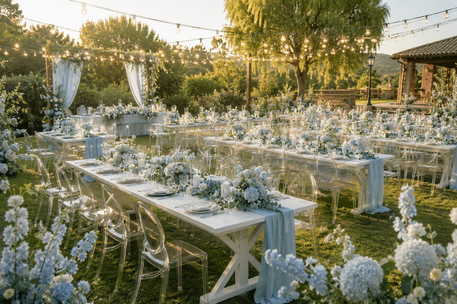 Pastel blue garden wedding reception featuring rustic farm tables, clear ghost chairs, floral centerpieces, and elegant outdoor event dining setup.