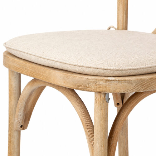 Close-up side view of beige linen-look seat cushion with piped edges on a natural wood cross back dining chair